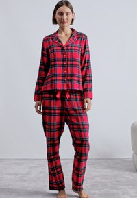 Rødrutete flanellpyjamas med knappesekk, krage og bukser med snor. Har svarte, grønne og blå linjer i et rutete mønster.
