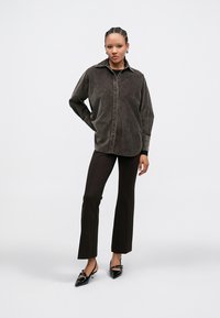 Brūns kordurojas krekla žakete ar apkakli, pogājamu priekšu un garām piedurknēm, kombinēta ar tumši brūnām biksēm ar zvana piegriezumu un melnām asām kurpēm.