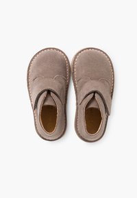 Scarpe per bambini in suede marrone con fibbia in velcro, forma arrotondata, cuciture a contrasto lungo la suola e rivestimento interno liscio.
