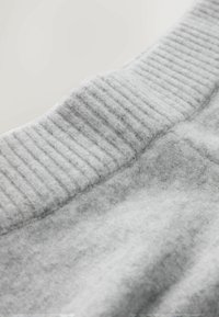 Pulover gri dintr-un material cu aspect texturat, având un decolteu ribat și un model subtil. Detaliu în prim-plan al articolelor vestimentare.