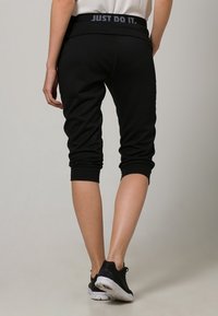 Joggers capri negros con una cinturilla texturizada que presenta el detalle "JUST DO IT." Las piernas son ajustadas y terminan justo debajo de la rodilla.
