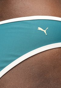 Τελ χαμηλό μαγιό σε τιρκουάζ με λευκή επένδυση, που φέρει λευκό λογότυπο Puma σε σκούρο καφέ δέρμα.