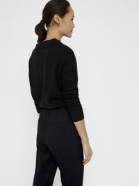 Jersey negro de corte relajado con puños acanalados, combinado con pantalones oscuros de cintura elástica y dos bolsillos traseros.