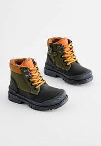 Bottes noires et vert olive avec des accents orange. Dotées d'une doublure en fausse fourrure texturée, de lacets jaunes et de semelles en caoutchouc durables avec du relief.