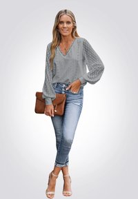 Gray blouse with eyelet detailing, V-neckline, and voluminous long sleeves. Paired with light blue distressed jeans and a brown clutch.