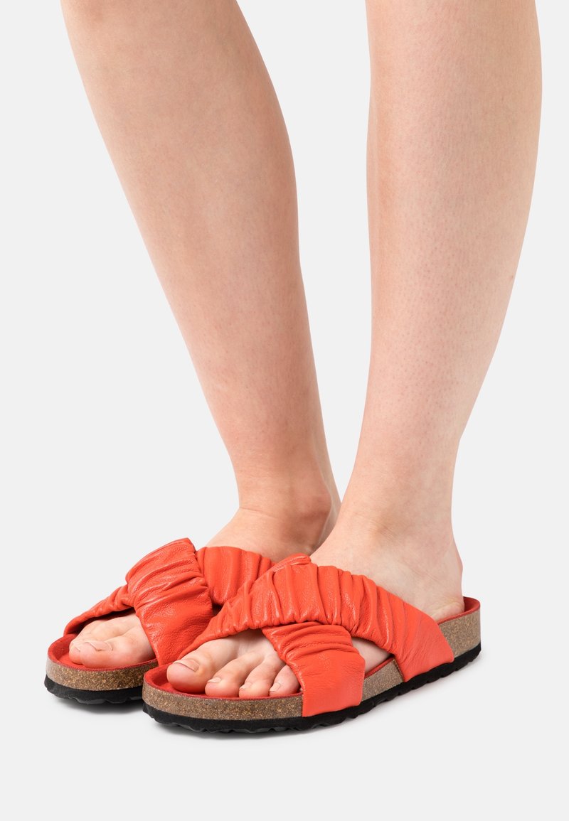Oranžové kožené sandály s uzlovým designem, polstrovanou stélkou, korkovou podrážkou a texturovanou černou podrážkou, které ukazují uvolněný, casual styl.