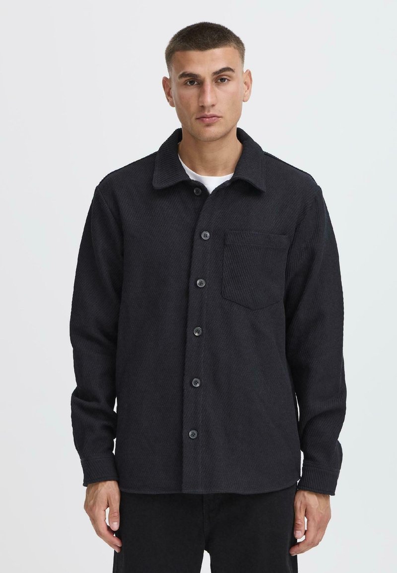 Black, textured shirt jacket with a collar, button closure, and front pocket. Features a ribbed pattern and long sleeves.