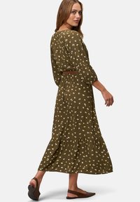 Maxi-Kleid aus olivgrüner Baumwolle mit weißen und gelben Blumenmustern, Dreiviertelärmel, taillierter Bund und gestufter Saum. Flache Sandalen.