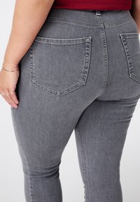 Jean en denim gris au design ajusté, avec deux poches arrière et une taille surpiquée. Le tissu a une texture lisse.