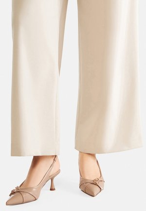Béžové lodičky na podpatku se stahovacími pásky, špičatou špičkou, raženým vzorem a malým zlatým detailem. Mají štíhlý podpatek a hladký lakovaný povrch.