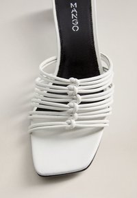 Sandale blanche à bout carré avec plusieurs fines lanières nouées et semelle intérieure noire estampillée "MANGO" sur un fond clair.