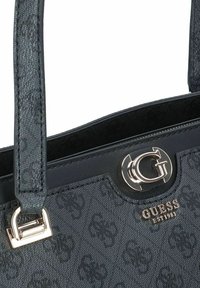 Zwarte handtas met een gestructureerd oppervlak en een opvallende zilveren sluiting met een 'G'-logo, gemarkeerd 'GUESS EST 1981', en een ontwerp met dubbele handgrepen.