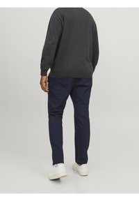 Mörkgrå stickad tröja med avslappnad passform, kombinerad med marinblå byxor i slät tyg och vita sneakers med strukturerade detaljer.