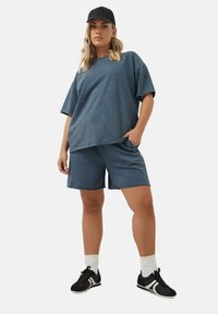 Niebieska, oversize'owa koszulka i dopasowane szorty z miękkiej mieszanki bawełny, charakteryzujące się swobodnym krojem, kieszeniami i gładką teksturą. Czarne sneakersy i czapka.