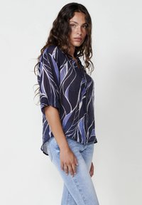 Blusa blu navy con motivo a foglie blu chiaro, maniche corte, taglio rilassato e orlo curvo, abbinata a jeans blu chiaro.