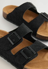 Mustmust ja kahe reguleeritava rihmaga mustad kootud sandaalid mustade metallist klambritega ning heledast pruunist pehmest tossust. Tekstuuriga ülemine pind.