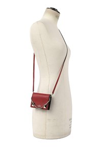 Sac bandoulière rouge et noir avec chaîne argentée et sangle d’épaule présenté sur un mannequin de couture blanc.