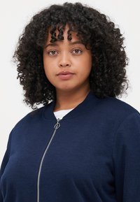 Navy blue zip-up bomber jacket with a round neckline, made of soft fabric. Features a silver zipper and ribbed cuffs.