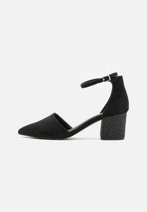 Chaussure à talon haut en suede noir avec un bout pointu, une bride à la cheville et un talon épais texturé. Design épuré avec un minimum de détails.