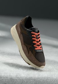 Sneaker caratterizzata da una combinazione di mesh nero e suede marrone, accentuata da lacci arancioni e una suola in gomma color crema per un look moderno.