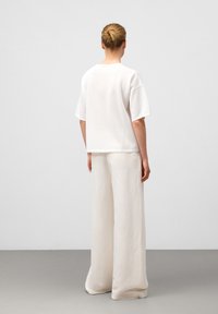 Witte katoenen oversized t-shirt met korte mouwen, gecombineerd met lichtbeige wijde broek, zachte textuur, minimalistisch ontwerp.