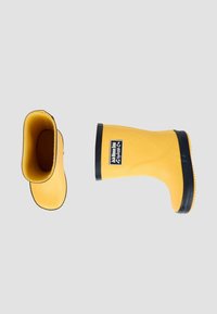 Bottes de pluie en caoutchouc jaunes avec semelles noires. Texture lisse, design courbé et larges ouvertures. Étiquette de logo sur le côté. Une botte affichée à l'envers.