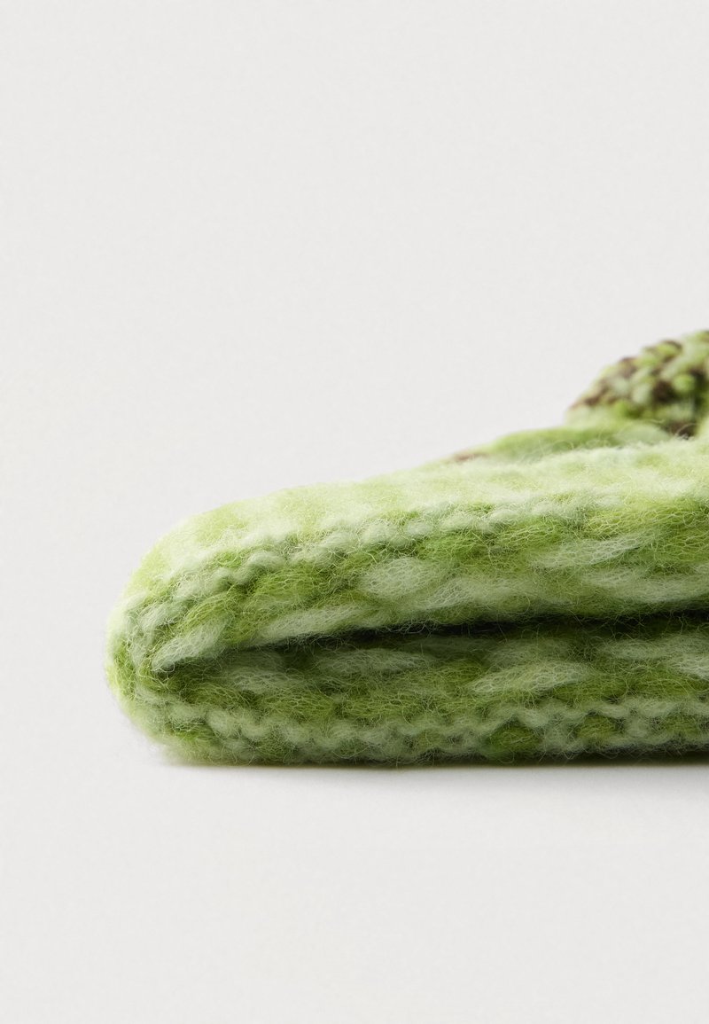 Grønt strikket tæppe lavet af blødt, struktureret stof med varierende nuancer af grøn og et tykt, chunky mønster.