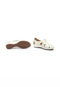 White leather shoes with crisscross straps and cut-out accents, featuring a textured brown rubber sole and stitched detailing around the edges.
