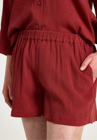 Röda texturerade shorts med elastisk midja. Innehåller sidofickor och en avslappnad passform, som framhäver en ribbad tygdesign.