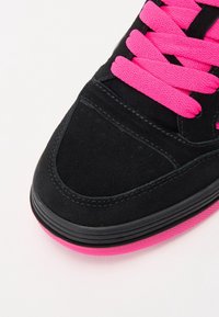 Baskets en daim noir avec des lacets rose vif et une semelle en caoutchouc rose. Présente des perforations sur la pointe et des coutures contrastées noires.