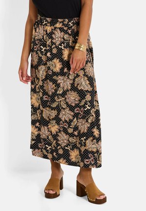 Jupe florale noire avec des motifs roses et dorés, ceinture élastique, design longueur cheville. Associée avec des sandales à talons épais marron.