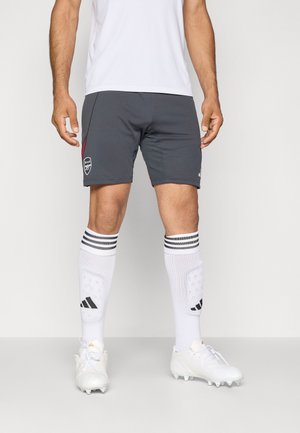 Grå sports shorts med røde detaljer, hvid trøje, hvide knælange sokker med sorte striber og hvide fodboldstøvler med strukturerede detaljer.