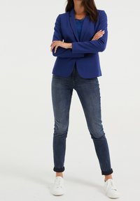Blå blazer med en en-knappsframsida, matchad med en blå topp med spetsdetaljer, slim fit mörka jeans och vita sneakers. Har en skräddarsydd passform.