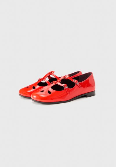 Red patent leather flats with cut-out detailing, two adjustable straps, and a low black sole. Smooth texture with a shiny finish.