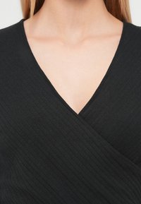 Top negro acanalado envolvente con un escote en V profundo y superficie texturizada. El tejido parece suave, con un diseño ceñido al cuerpo.