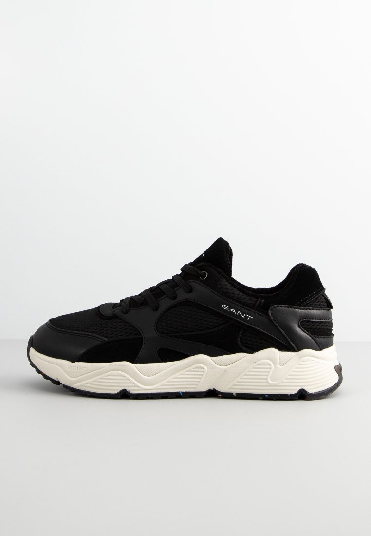 Schwarze Sneaker aus einer Kombination von glatten und strukturierten Materialien, mit einer dicken, cremefarbenen Sohle und dezentem lateralem Branding an der Seite.