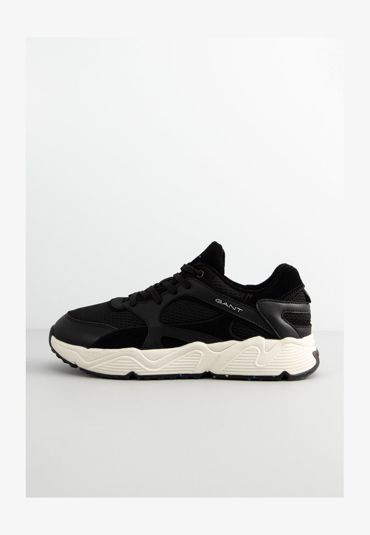 Schwarze Sneaker aus einer Kombination von glatten und strukturierten Materialien, mit einer dicken, cremefarbenen Sohle und dezentem lateralem Branding an der Seite.