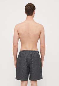 Shorts a rayas en blanco y negro con una cinturilla elástica y dos bolsillos traseros. Costuras visibles que acentúan el diseño y un ajuste casual.
