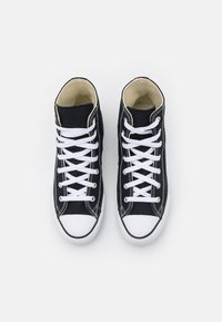 Sorte høy-hælte sneakers med hvite snørebånd, gummitåhette og sømdetaljer. Lages i canvas-materiale med en kontrasterende beige fôr.
