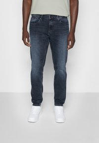 Mörkblå denim jeans med rak benmodell och lätt blekning, med framfickor och knappstängning, kombinerat med vita sneakers.