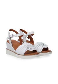 Witte wedge sandalen met een geknoopte voorkant en kruisbandontwerp, met een bruine leren inlegzool en een gestructureerde witte zool.