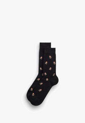 Černé ponožky zdobené malými perníkovými panáčky s červenými čepicemi Santa, uspořádané vedle sebe na bílém pozadí.