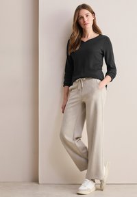 Schwarzes Langarmoberteil mit V-Ausschnitt, kombiniert mit hellbeigen, weiten Jogginghosen. Weiße Sneakers vervollständigen das Outfit.