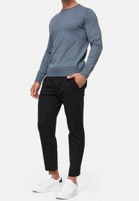 Helles blauer langärmliger Pullover mit geripptem Ausschnitt; kombiniert mit schwarzen schmal zulaufenden Hosen und weißen Sneakern mit schwarzen Akzenten.