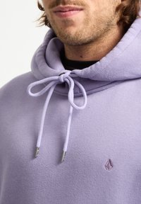 Hoodie lavande en tissu doux avec une capuche à cordon de serrage, des embouts métalliques et un petit logo brodé sur la poitrine.