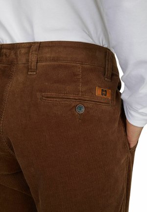 Braune Cordhosen mit vertikaler Rippstruktur, ausgestattet mit einer Gesäßtasche, Knopfverschluss und einem Leder-Logo-Label am Bund.