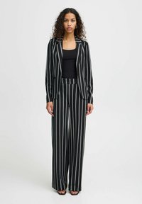 Costume à rayures noir et blanc comprenant un blazer ajusté et un pantalon large. Le tissu a une texture lisse et un éclat subtil.
