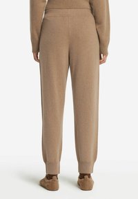Bruna stickade mjukisbyxor med en avslappnad passform, smalnande cuffs och resårmidja, med en mjuk textur och inga synliga mönster.