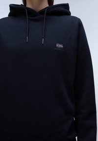 Sudadera azul marino hecha de tela suave, con un bolsillo tipo canguro en la parte frontal, capucha con cordón y un pequeño logo bordado en el pecho.