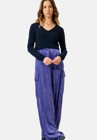 Navyfarbener V-Ausschnitt-Pullover und lila gerippte weite Hosen mit Cargo-Taschen. Glatte Textur, lässige Passform und minimalistisches Design.